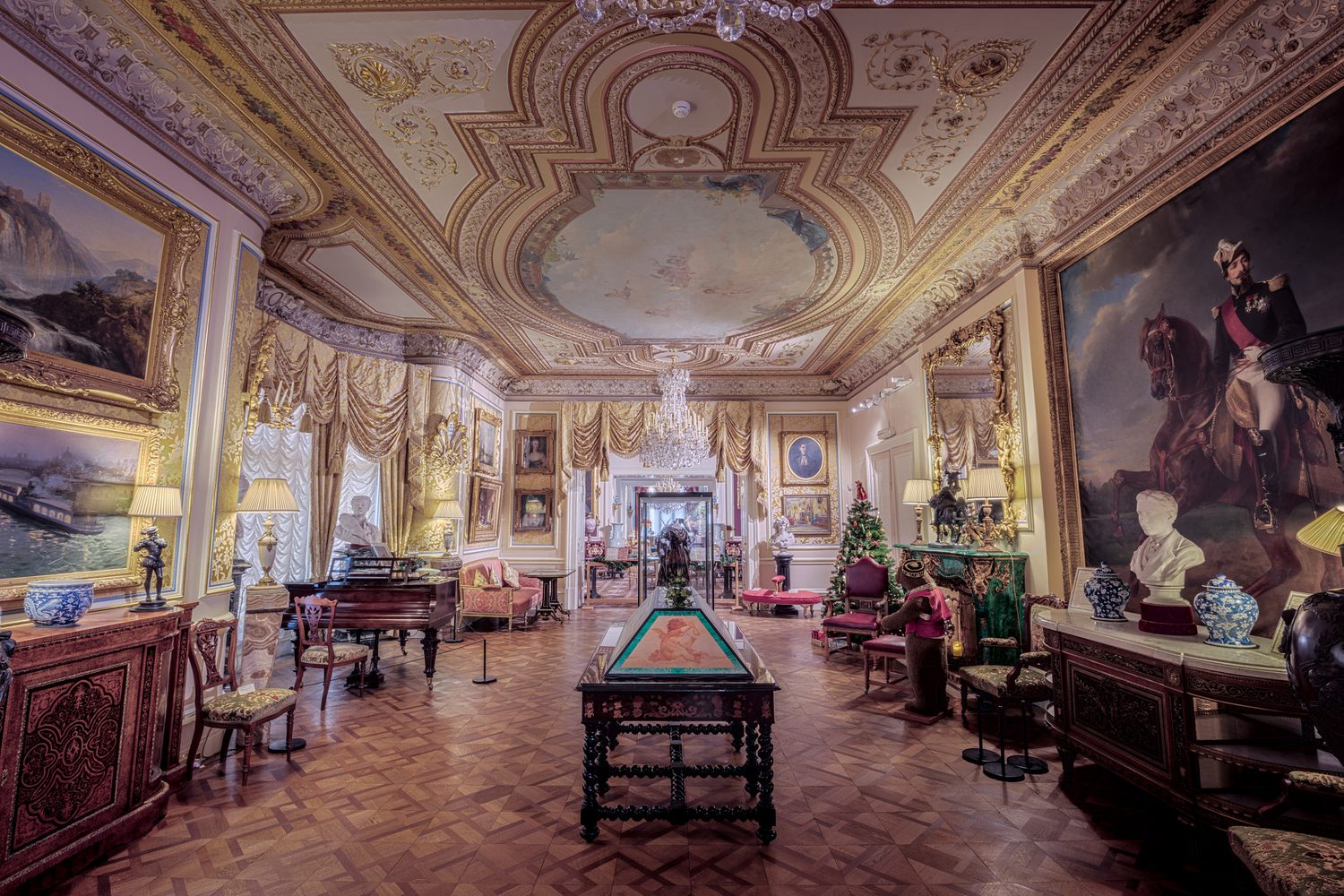 A grand, antique-filled estate drawing room with a grand piano, oil paintings, and chandeliers